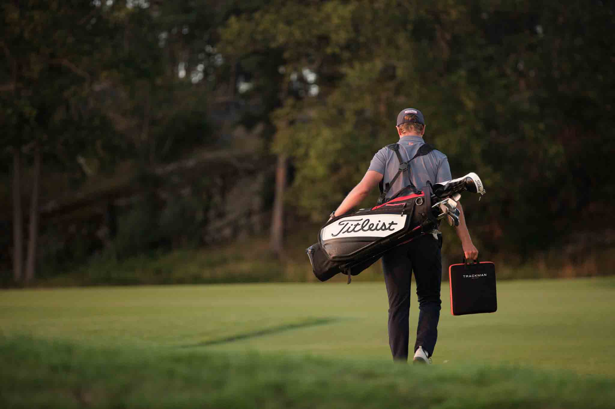 A golfer walking off the course with a golf bag full of clubs from a professional Tee Box club fitting.