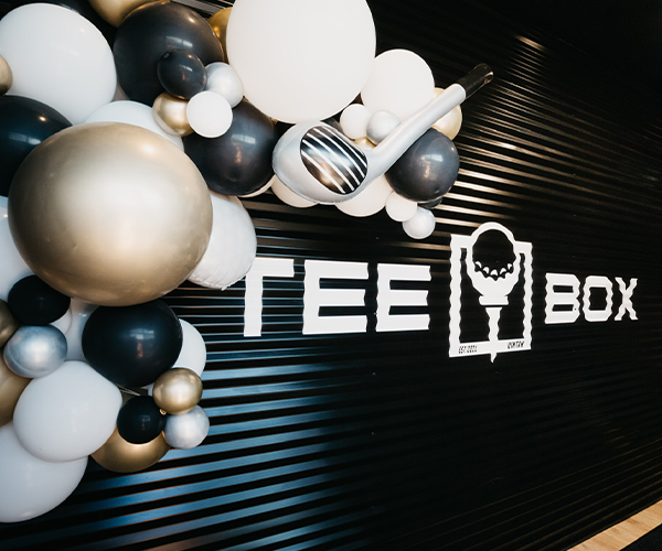 An image of a Tee Box sign with party balloons hanging over it - contact for more information about our party venues.