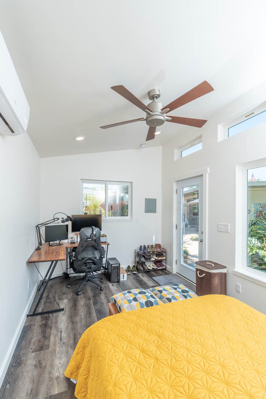 A modern home with dark floors with a desk and bed, provided by one of the best affordable tiny home builders.